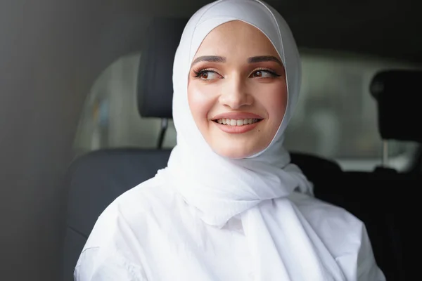 Schöne muslimische Frau im weißen Hijab sitzt auf dem Rücksitz eines Luxusautos — Stockfoto