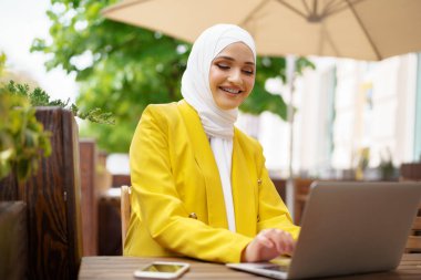 Kafede laptopuyla gülümseyen güzel Müslüman kadın.