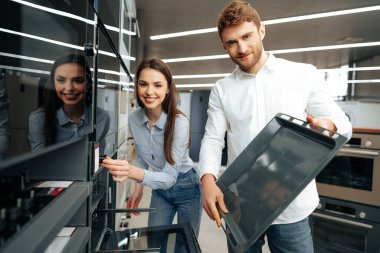 Genç çift hipermarkette yeni elektrikli fırın seçiyor.