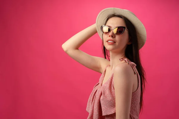 Studio fashion portrait of a young attractive woman in hat and glasses against pink backgorund — Stock Photo, Image