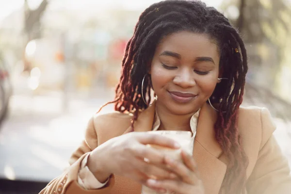 Hermosa joven afroamericana mujer sentada en la cafetería al aire libre y beber café — Foto de Stock