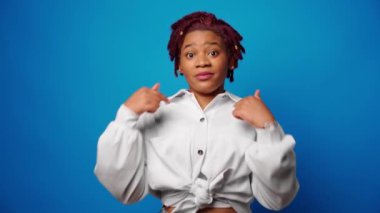 Heyecanlı genç afro kadın kendini gösteriyor, başarıyla mutlu, kazanan, mavi arka planda.