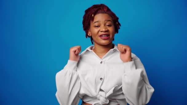 Fajna młoda afro kobieta pokazuje kciuki do góry, zatwierdza coś, niebieskie tło — Wideo stockowe