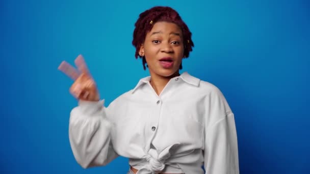 Glädjande glad afro kvinna visar seger tecken mot blå backgorund — Stockvideo