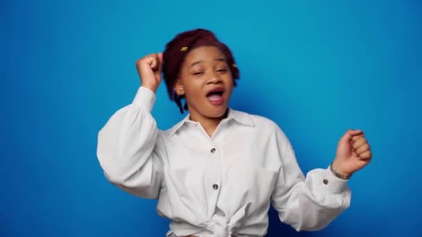 Boldog fiatal afro-amerikai nő táncol a stúdióban a kék háttér — Stock videók