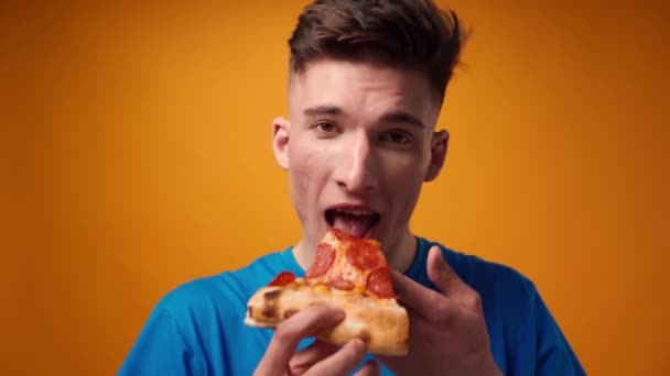 Primer plano de un tipo comiendo rebanada de pizza contra fondo de estudio amarillo — Vídeos de Stock