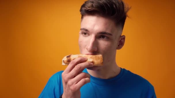 Close-up van een man eten pizza slice tegen gele studio achtergrond — Stockvideo
