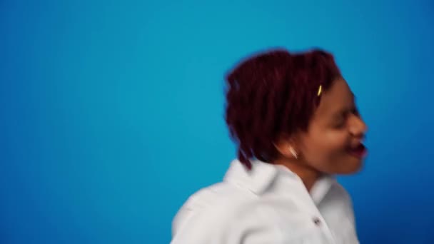 Glad ung afro amerikansk kvinna dansar i studio mot blå bakgrund — Stockvideo