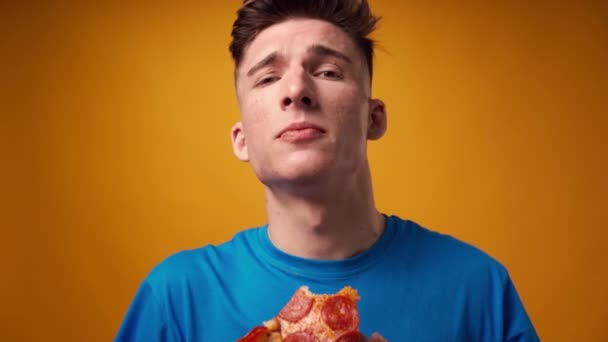 Dekat dari seorang pria makan pizza slice terhadap latar belakang studio kuning — Stok Video