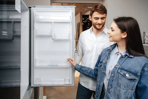 Pareja joven seleccionando nuevo refrigerador en la tienda de electrodomésticos — Foto de Stock