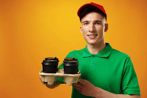 Fiatal futár kezében kávéscsészék sárga háttér — Stock Fotó
