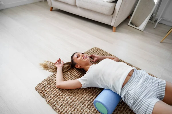 Young woman doing exercise with gymnastic roll on the floor at home — Stock Photo, Image