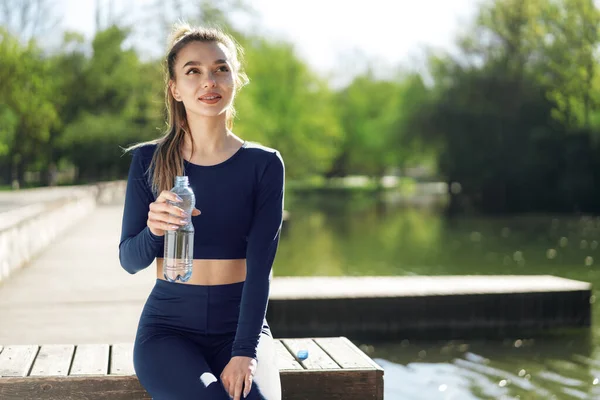 Retrato de una joven hermosa mujer con ropa deportiva azul bebiendo agua en el parque — Foto de Stock