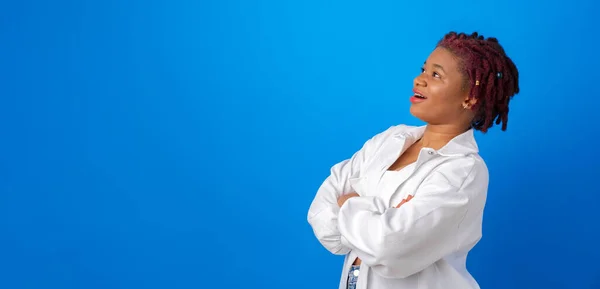 Молода афро-жінка в білій сорочці дивиться на місце для копіювання реклами на синьому фоні — стокове фото