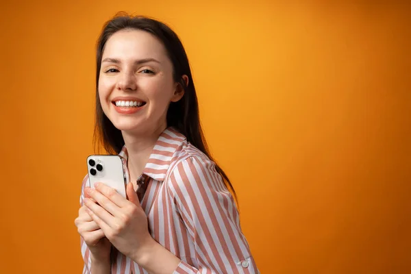 Porträt einer jungen attraktiven Frau, die ihr Smartphone vor gelbem Hintergrund benutzt — Stockfoto