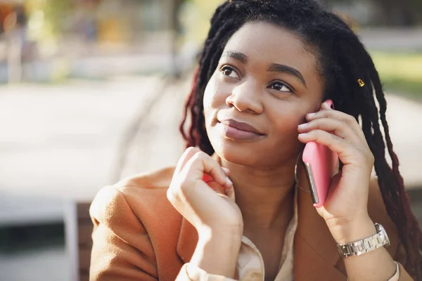 Positivo joven negro mujer sentado en la cafetería al aire libre y tomar en el teléfono — Foto de Stock