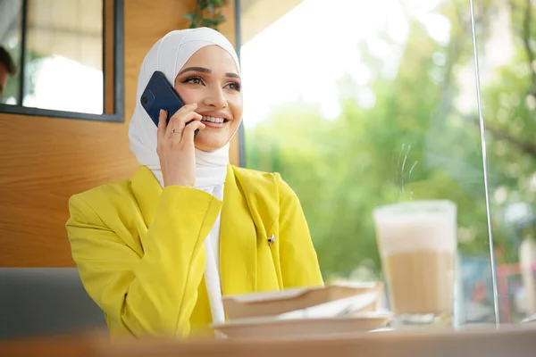 Jonge moslim zakenvrouw in hoofddoek zitten in cafe en praten aan de telefoon — Stockfoto