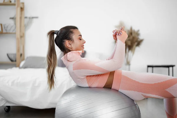 家でフィットネスボールの上で腹筋の練習を行うスポーティ女性 — ストック写真