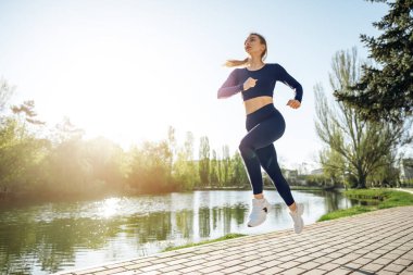 Atletik formda genç bir kadın sabah parkta koşuyor.
