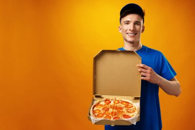 Sarı arka planda pizza kutusunu tutan mutlu teslimatçı.