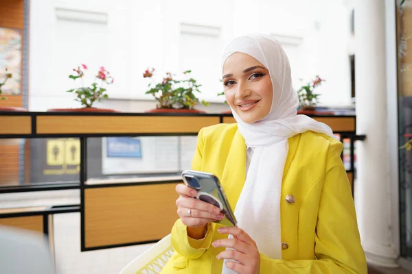 年轻的穆斯林妇女在咖啡店里用她的智能手机 — 图库照片