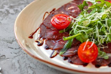 Gri yüzeyde roka ve parmesanlı biftek carpaccio.