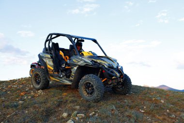 Kasklı bir adam dağlarda ATV bisikletinin üzerinde oturuyor.