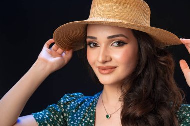 Hasır şapkalı, siyah arka planda poz veren güzel bir genç kadın.