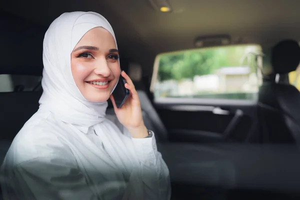 Schöne junge Frau im Hijab sitzt im Auto und telefoniert — Stockfoto