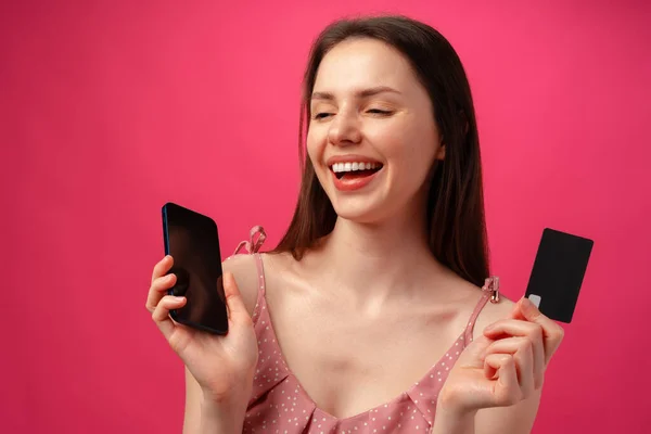 Sorridente giovane donna in possesso di smartphone e carta di credito contro sfondo rosa — Foto Stock