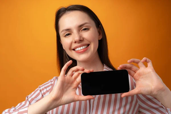 Glücklich lächelnde junge Frau zeigt Ihnen schwarzen Smartphone-Bildschirm mit Kopierraum — Stockfoto