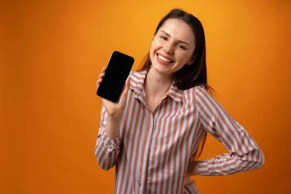 Feliz sorrindo jovem mulher mostrando-lhe tela de smartphone preto com espaço de cópia — Fotografia de Stock