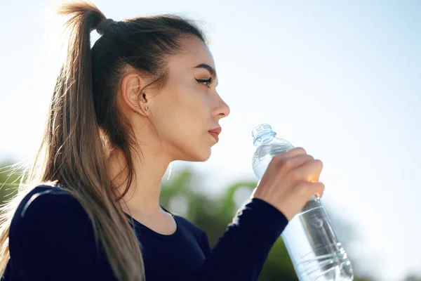 Retrato de jovem mulher bonita vestindo azul sportswear água potável no parque — Fotografia de Stock