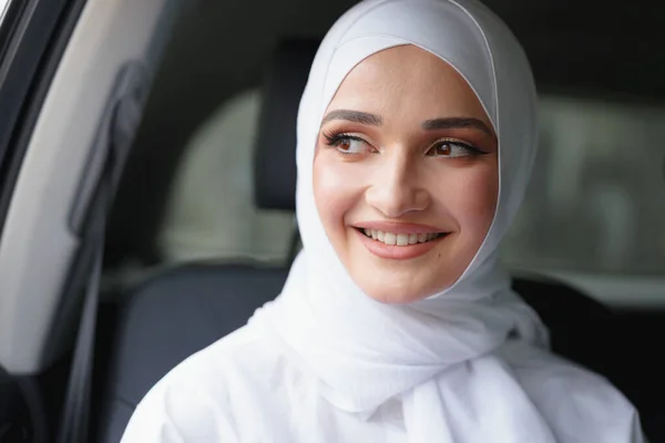 Gyönyörű muszlim nő fehér hidzsábban ül egy luxusautó hátsó ülésén. — Stock Fotó