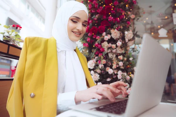 Mooie jonge moslim vrouw met behulp van laptop tijdens het zitten in cafe — Stockfoto