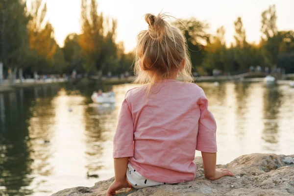 Petite fille assise sur une énorme pierre dans le parc près du lac — Photo