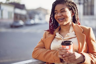 Afrika kökenli Amerikalı bir kadın elinde kahve fincanı ile srteet 'te duruyor.