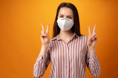 Sarı arka planda tıbbi maske takan güzel bir kadının stüdyo portresi.