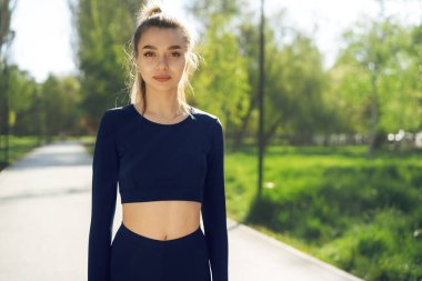 Sabah parkında spor giyinmiş gülümseyen genç bir kadının portresi.