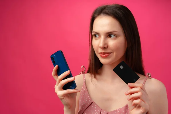 Sorrindo jovem segurando smartphone e cartão de crédito contra backgorund rosa — Fotografia de Stock