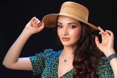 Hasır şapkalı, siyah arka planda poz veren güzel bir genç kadın.