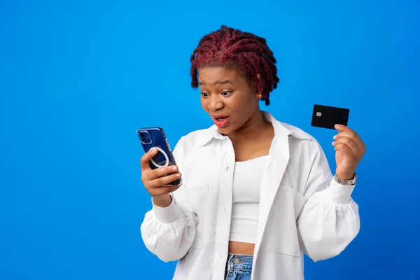 Африканська американка тримає смартфон і кредитну картку на синьому фоні. — стокове фото