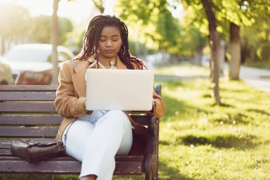 Afrikalı Amerikalı kadın bir bankta oturuyor ve dizüstü bilgisayar kullanıyor.