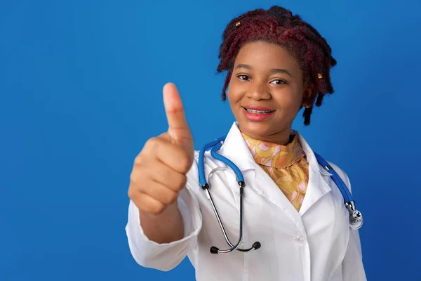 Ung afrikansk amerikansk kvinna läkare visar ok tecken mot blå bakgrund — Stockfoto