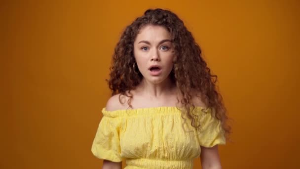 Mladá kudrnatá žena zklamaná a šokovaná špatnou zprávou, žluté pozadí — Stock video