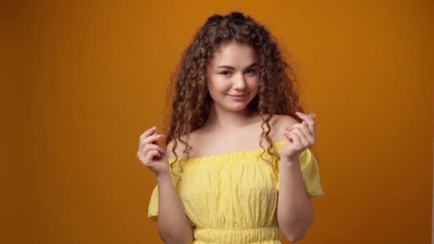 Ung kvinna gnugga fingrar i pengar gest mot gul bakgrund — Stockvideo