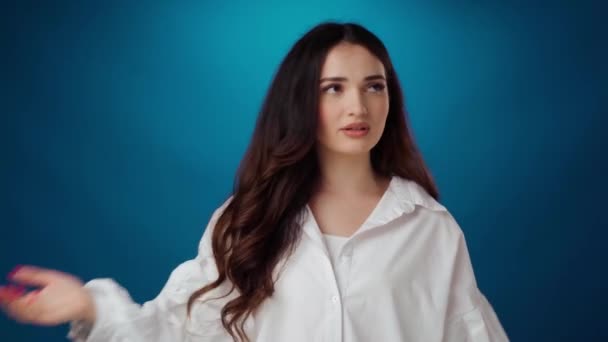 Irriteret ung brunette kvinde skælder nogen på blå baggrund – Stock-video