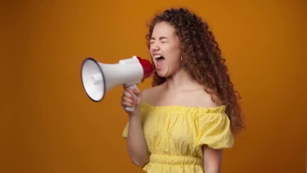 Kręcone włosy młoda kobieta krzyczy do głośnika na żółtym tle — Wideo stockowe