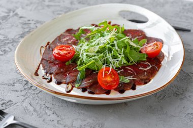 Gri yüzeyde roka ve parmesanlı biftek carpaccio.