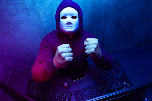 Hacker anónimo con máscara facial que trabaja en la computadora en la habitación oscura —  Fotos de Stock